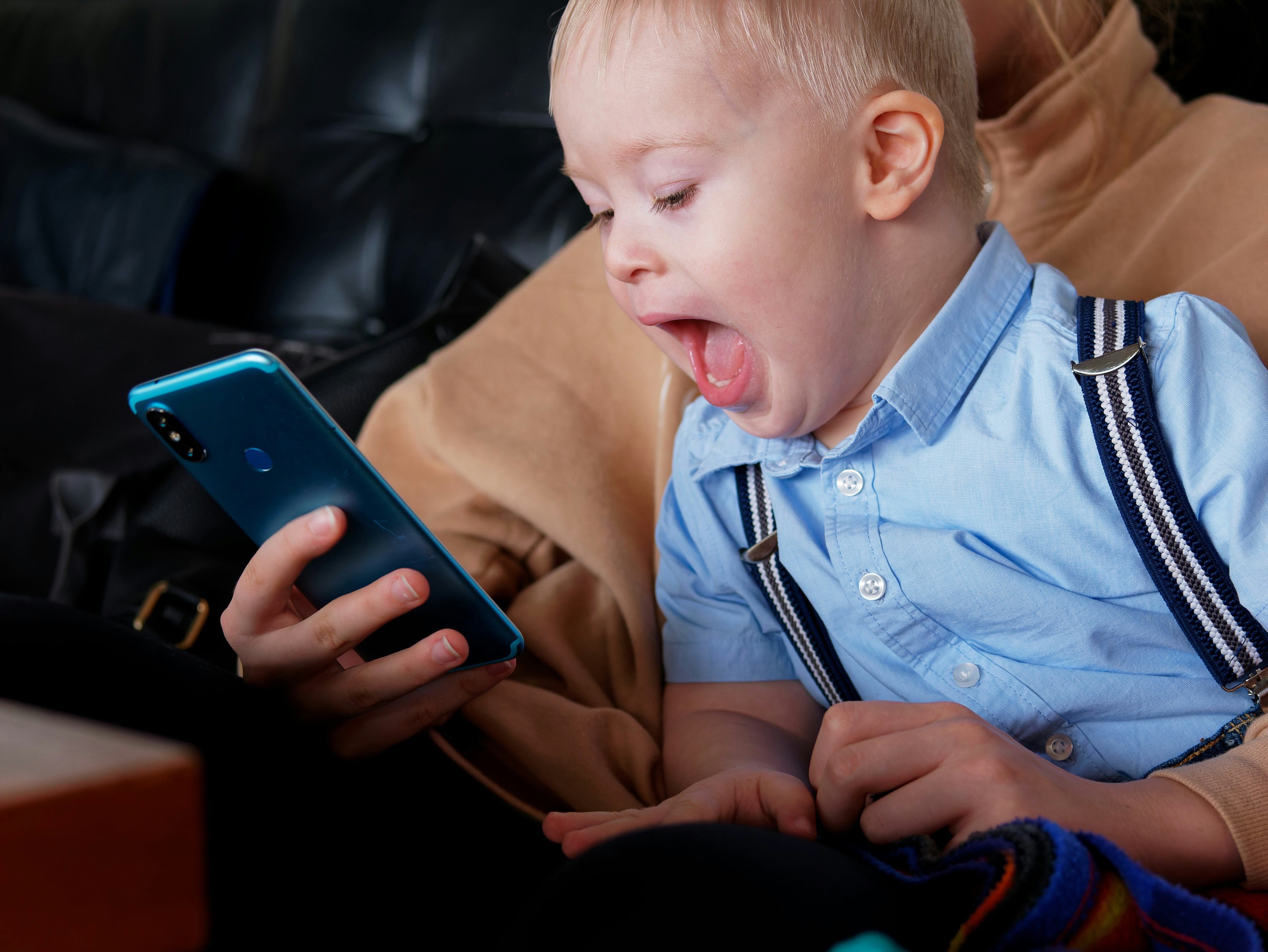 A parent and a young child sitting together on a couch, smiling as they interact with a tablet.