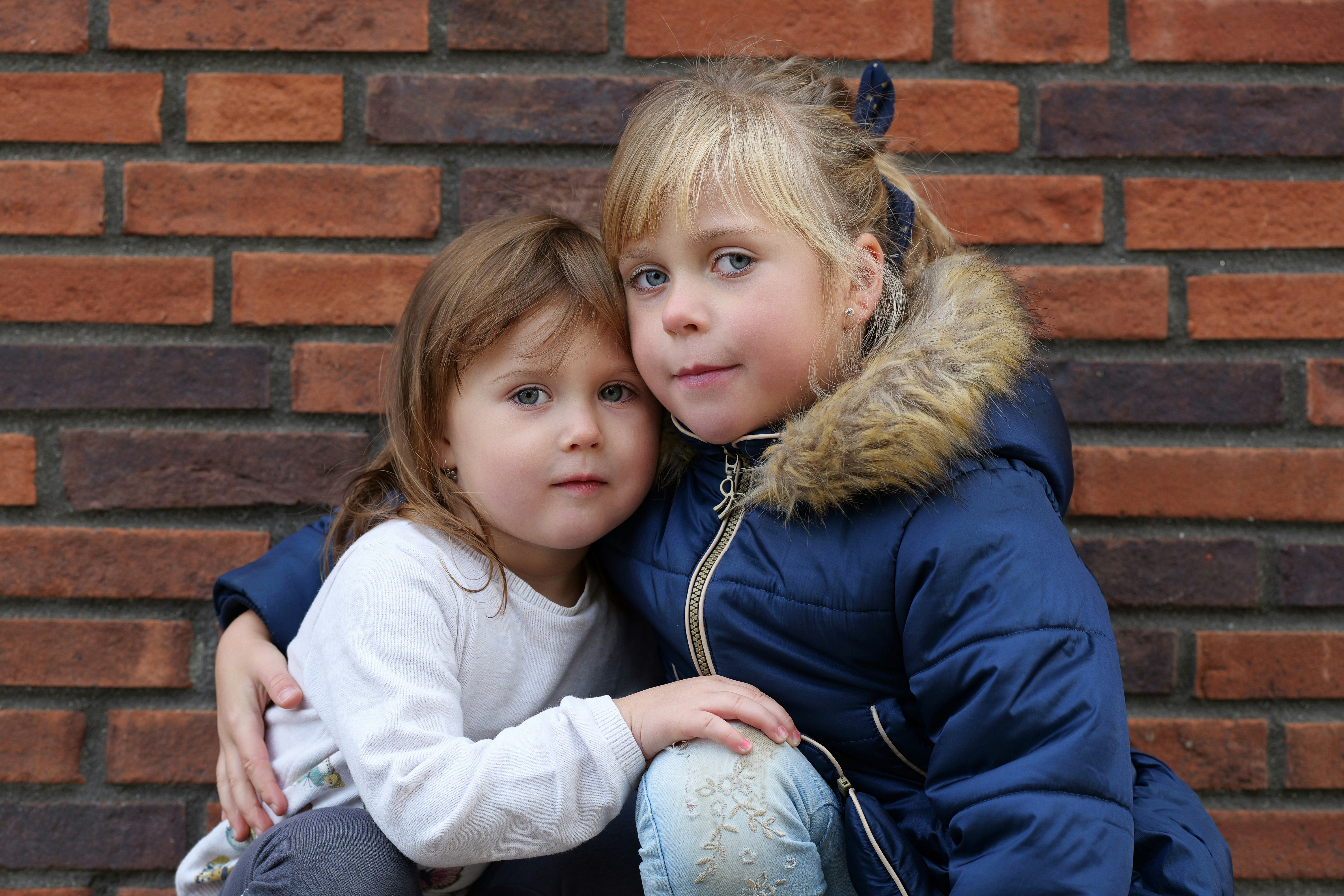 Two young children sitting close together, one appears to be comforting the other by putting a hand on their shoulder.